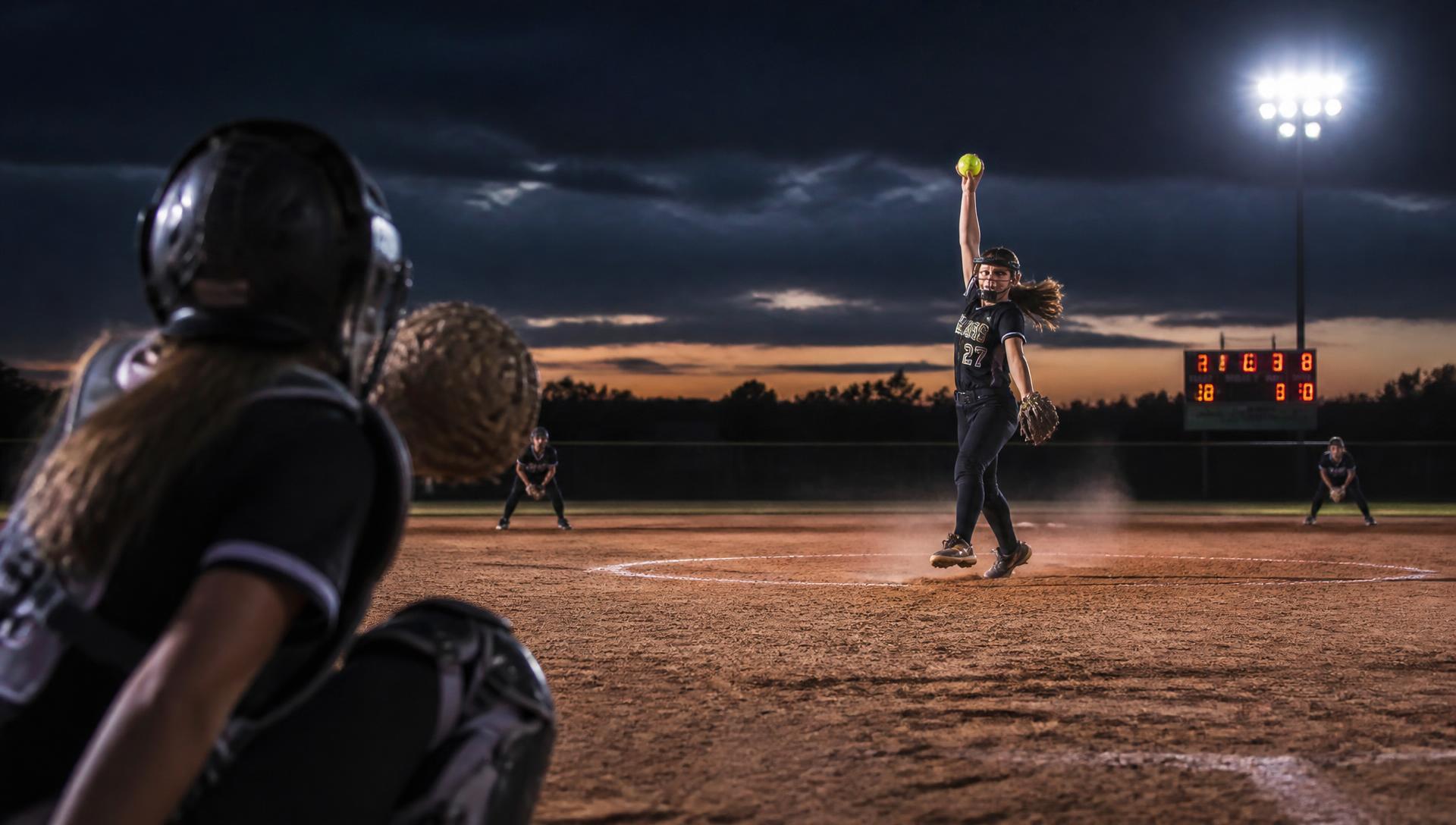 Middle school softball pitcher mid-windup under the lights
